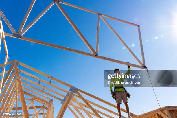 a framer standing on the skelton framed walls of a new home construction guiding the crane operator to set another truss - roof truss stock pictures, royalty-free photos & images
