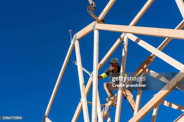 a framer standing on the framed walls of a new home construction guiding the crane operator to set another truss - roof truss stock pictures, royalty-free photos & images