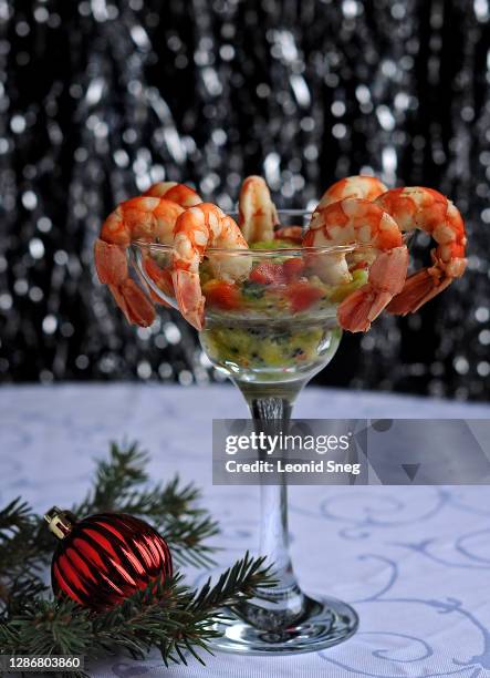 food photography of salad shrimp cocktail with guacomole christmas dish, side view, closeup appetizer in a tall glass goblet on a dark shiny background with red new year decorations - garnele stock-fotos und bilder