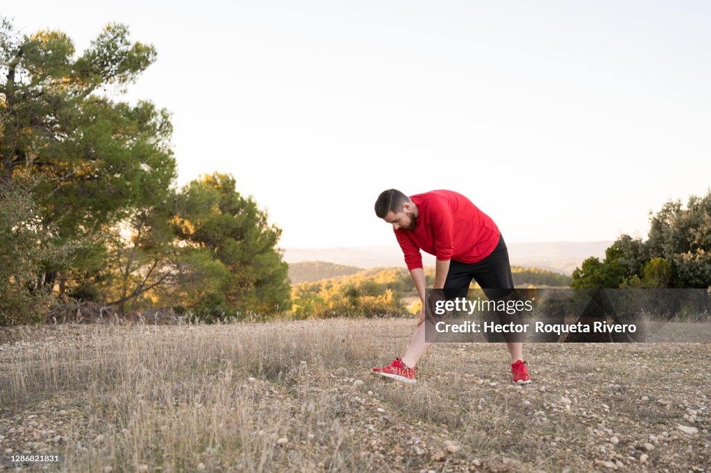 Young caucasian man with beard, brown hair and red sportswear practicing sport exercise in the field. Healthy life concept