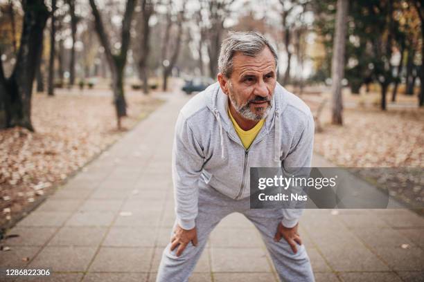 a portrait of a man with a beard doing muscle stretching exercises in a public park - guy looking down stock pictures, royalty-free photos & images