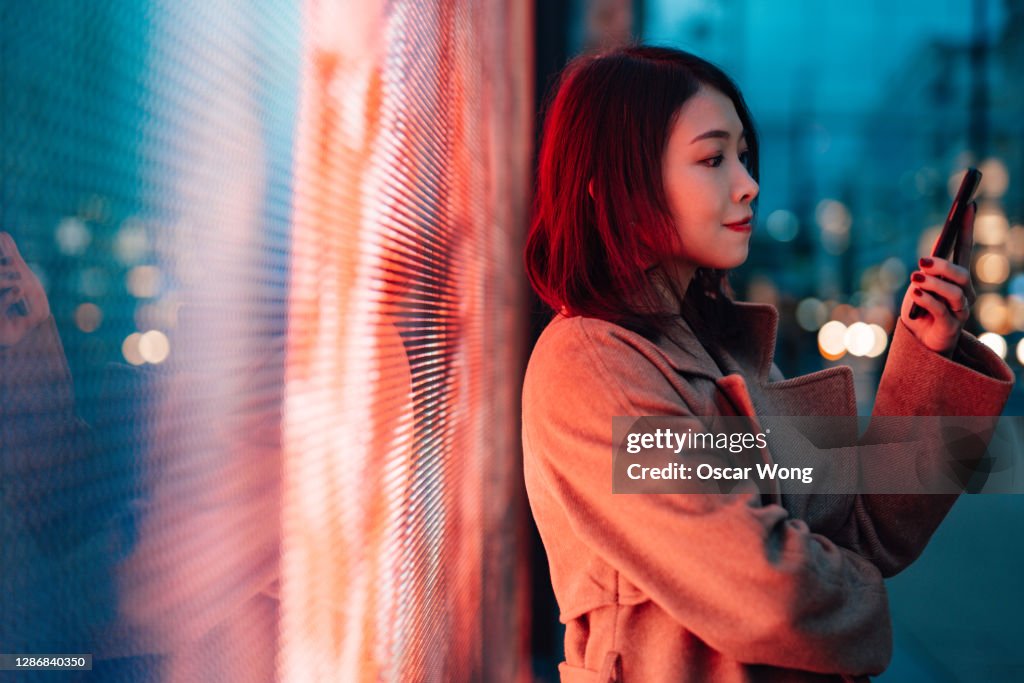 The Future Of Digital World - Young Woman With Smartphone Standing Against A Digital Display.