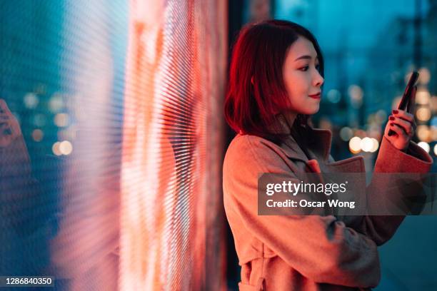 the future of digital world - young woman with smartphone standing against a digital display. - colorful lights fotografías e imágenes de stock