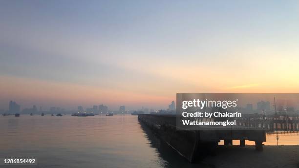 far side of pattaya beach in the early morning with beautiful sky, many fishing boated moored in the bay with cityscape of pattaya in the mist of pm2.5 air pollution. - man mist beach stock-fotos und bilder