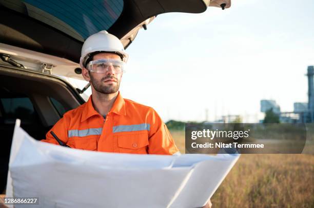 project engineer sitting at the car trunk while working with blueprint or project task follow up at construction site outdoors. - task force stockfoto's en -beelden