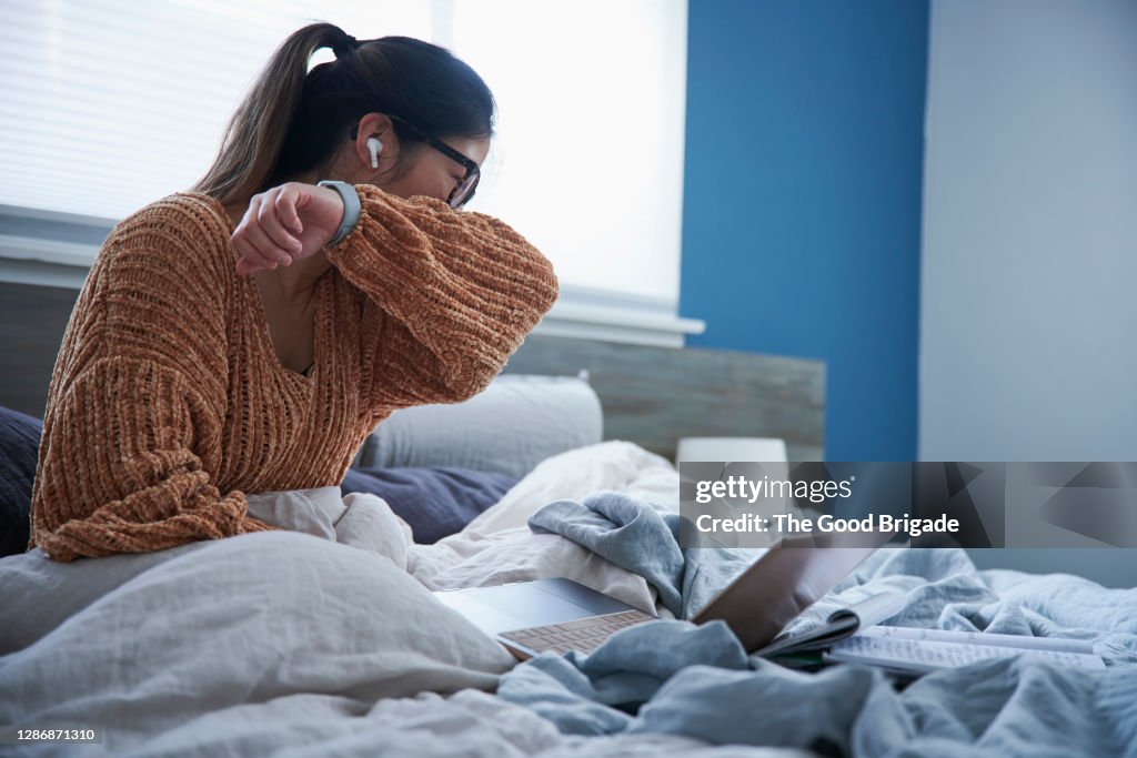 Woman coughing into elbow while sitting in bed
