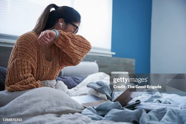 woman coughing into elbow while sitting in bed - tousser photos et images de collection