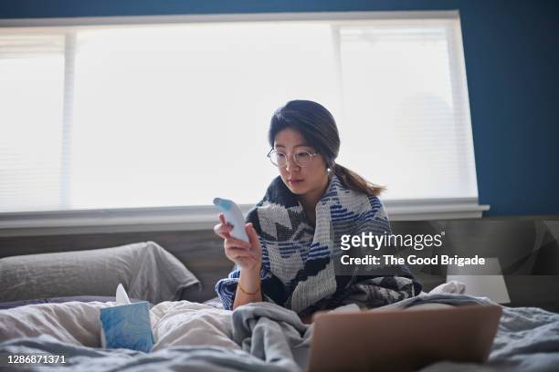 woman taking temperature in bed with digital thermometer - digital thermometer stock pictures, royalty-free photos & images