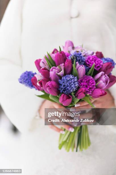 a beautiful bouquet of bright multicolored flowers in the hands of a girl or woman. a bride in an elegant dress and a white fur coat holds a wedding bouquet in her hands. - winter wedding stock pictures, royalty-free photos & images