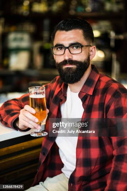 hipster in bar drinking alcohol. beer and tapas. posing serious with ambient light looking at view - socialist international stock pictures, royalty-free photos & images