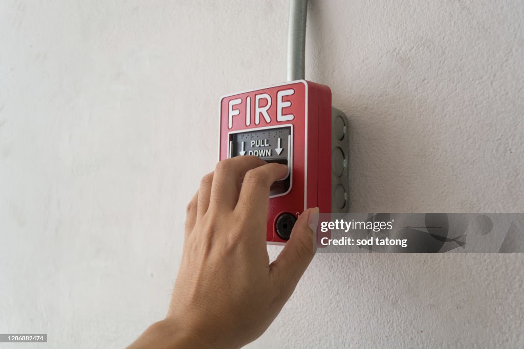 The hand of man is pulling fire alarm on the wall next to the door