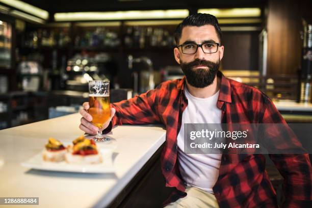 hipster in bar drinking alcohol. beer and tapas. posing serious with glass of beer - socialist international stock pictures, royalty-free photos & images