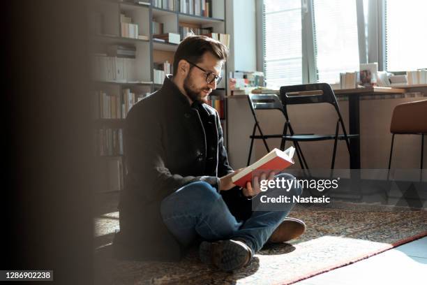 young man enjoying an interesting book sitting on floor - self improvement stock pictures, royalty-free photos & images