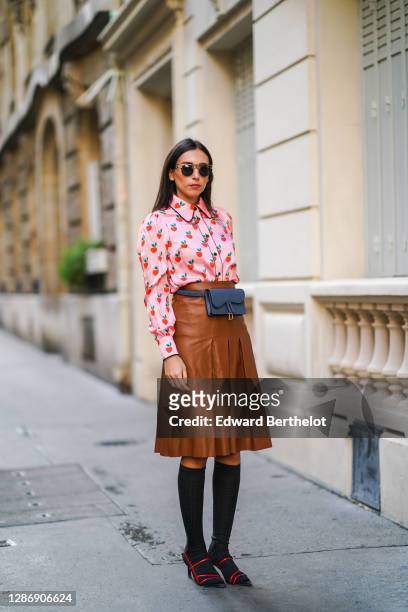 Gabriella Berdugo wears a preppy pink shirt with printed strawberry details, a midi pleated / gathered leather brown skirt from Manoush, black long...