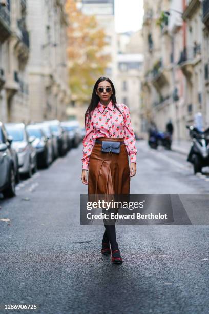 Gabriella Berdugo wears a preppy pink shirt with printed strawberry details, a midi pleated / gathered leather brown skirt from Manoush, black long...