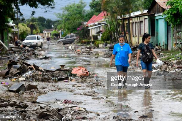 Two women walk with rubber boots over a mud-covered street with debris left by Hurricane Iota flooding at Colonia Celeo Gonzales on November 21, 2020...