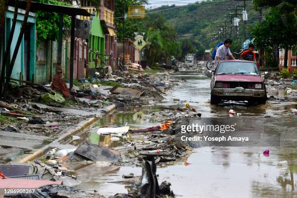 Group of people on a car drive through a mud-covered street with debris caused by Hurricane Iota's flooding on November 21, 2020 in San Pedro Sula,...