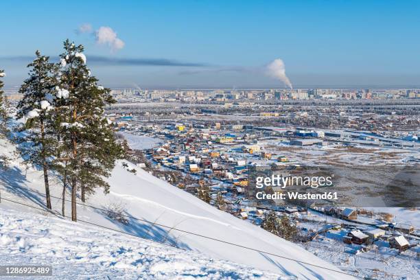 russia, republic of sakha, yakutsk, snowcapped hill with city houses in background - siberia imagens e fotografias de stock
