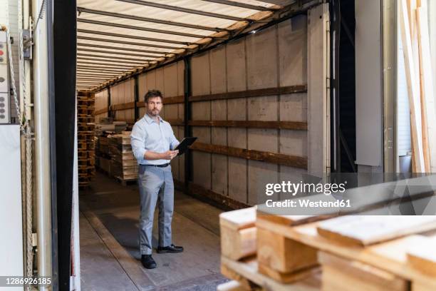 inspector with digital tablet loading material while standing in delivery truck - delivery truck stock-fotos und bilder