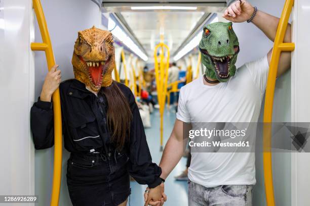 male and female friends holding hands while wearing dinosaur mask in train - bizarre fotografías e imágenes de stock