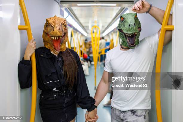 male and female friends holding hands while wearing dinosaur mask in train - animals and people imagens e fotografias de stock