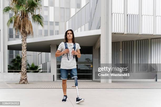 man with artificial limb walking against building in city - amputé photos et images de collection