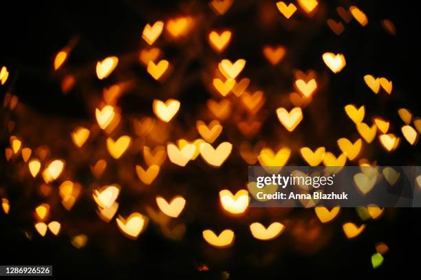 defocused yellow warm golden lights in shape of heart blurred bokeh. festive black christmas or new year background. - black and gold heart stock pictures, royalty-free photos & images