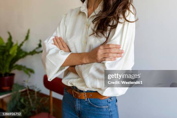 woman wearing white shirt with arms crossed standing against wall at home - white women stock pictures, royalty-free photos & images