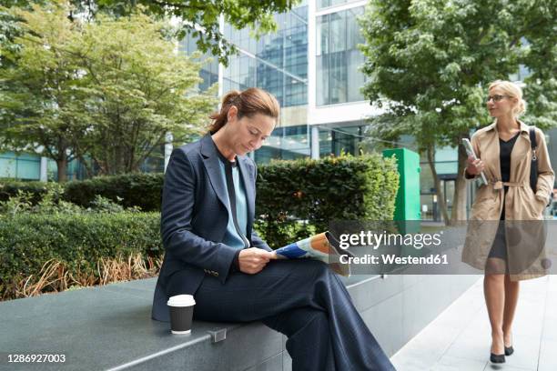 businesswoman reading paper with colleague leaving after work at city - business park uk stock pictures, royalty-free photos & images