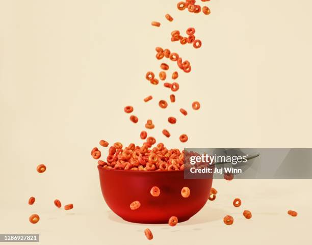 red cereal pouring into a red bowl with spoon on cream background - cereal bowl stockfoto's en -beelden