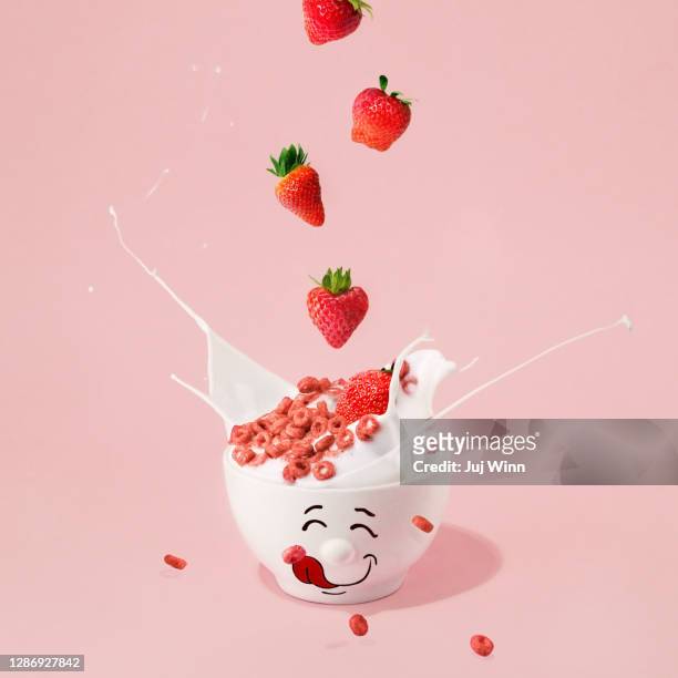 strawberries falling into a bowl of cereal and milk - strawberry falling stock-fotos und bilder