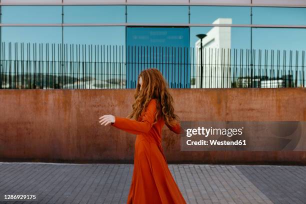 happy young woman dancing on footpath by surrounding wall - red dress stock pictures, royalty-free photos & images