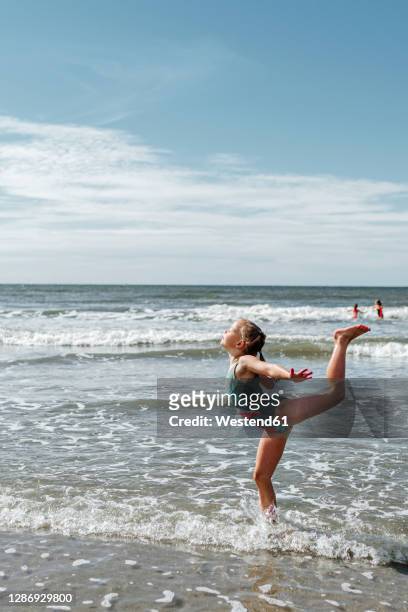 girl doing gymnastics while standing in water at beach on sunny day - dar uma ajuda imagens e fotografias de stock
