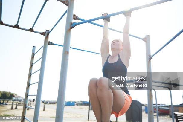 sports female doing pull ups in outdoor gym on sunny day - reck stock-fotos und bilder