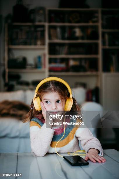 girl wearing headphones looking away while leaning on table at home - kid listening stock pictures, royalty-free photos & images