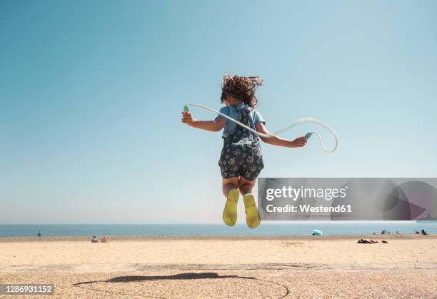 girl playing with skipping rope while jumping on beach against clear sky - back in the game stock pictures, royalty-free photos & images