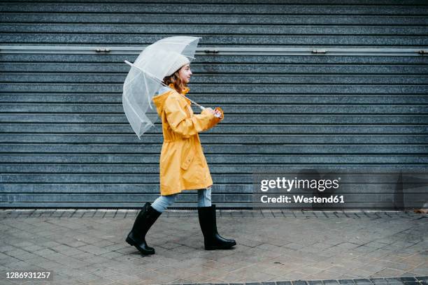 girl wearing raincoat and jump boot holding umbrella while walking on sidewalk - girl shower stock pictures, royalty-free photos & images