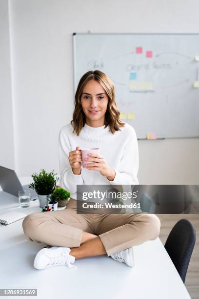 young businesswoman drinking coffee while sitting on table at office - pause café bureau photos et images de collection