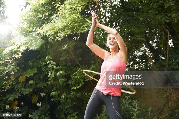 active senior spinning hula hoop while standing in back yard on sunny day - jogar ao arco imagens e fotografias de stock