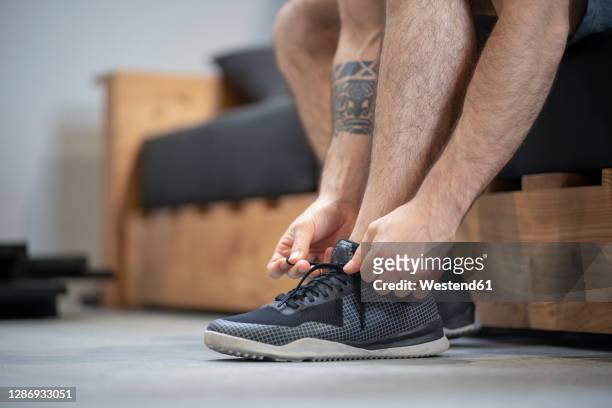 close-up of man tying shoelace while sitting on bed at home - amarrado imagens e fotografias de stock