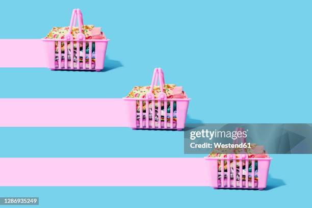 studio shot of three pink shopping baskets filled with clothing leaving pink trails - traje completo imagens e fotografias de stock