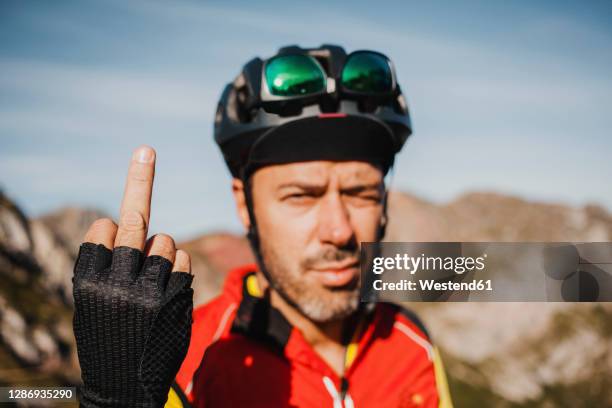 mid adult man showing middle finger while standing against mountain at somiedo natural park, spain - doigt dhonneur stockfoto's en -beelden