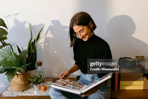 smiling woman looking photographs in photo album while sitting at home - looking at a photo album stock-fotos und bilder