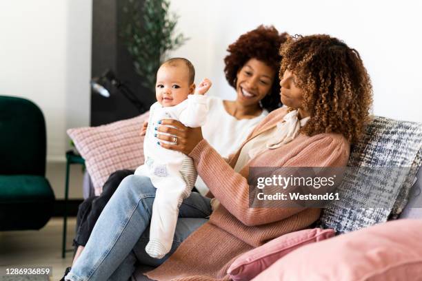 smiling family sitting with baby girl on sofa at home - aunt ストックフォトと画像