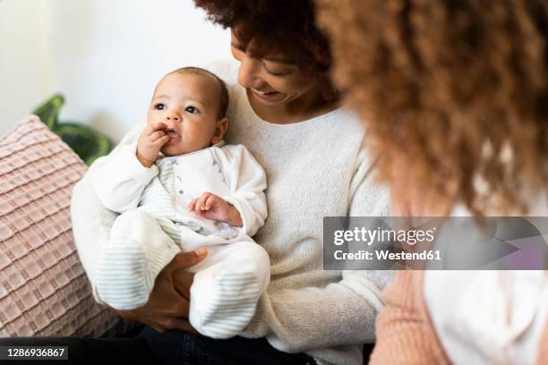 aunt holding niece while mother sitting beside at home - niece fotografías e imágenes de stock