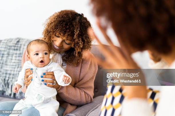 female toddler looking at aunt doing hand gesture sitting on sofa in living room - aunyy stock pictures, royalty-free photos & images