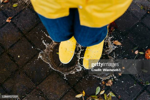 woman wearing yellow boots jumping on puddle during rainy season - cobblestone puddle stock pictures, royalty-free photos & images