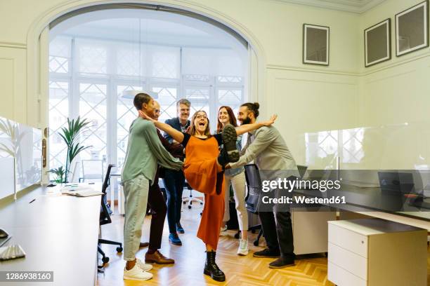 cheerful businesswoman falling while coworkers catching at workplace - trust fotografías e imágenes de stock