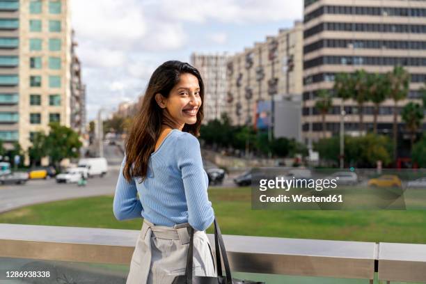 smiling beautiful businesswoman standing by railing while city in background - looking behind stock pictures, royalty-free photos & images