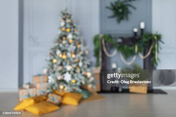 blurred bokeh background of christmas fir tree near fireplace with mahy yellow pillows and gift boxes - christmas still life stock-fotos und bilder